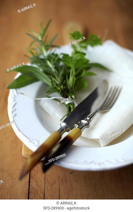 A bouquet of herbs on a plate with a serviette and cutlery