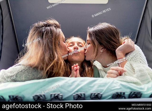 Friends kissing woman lying on bed in camper van