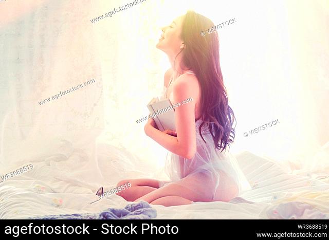 Holding the book sexy young woman sitting on the bed