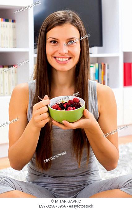 Happy young woman holding cereal with fruits in bowl at home. Healthy Food and Dieting concept
