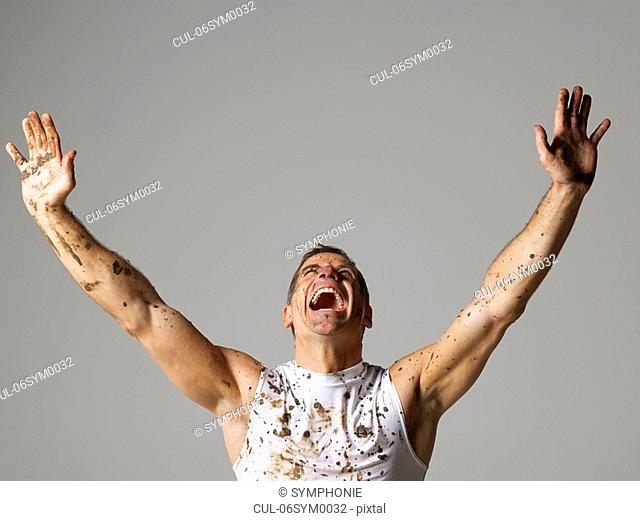 Joyous mud covered man with arms raised