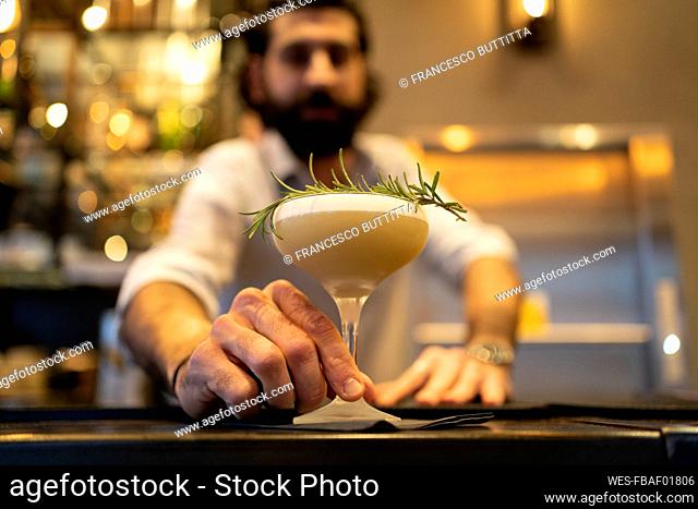Waiter giving thyme garnished drink at bar counter