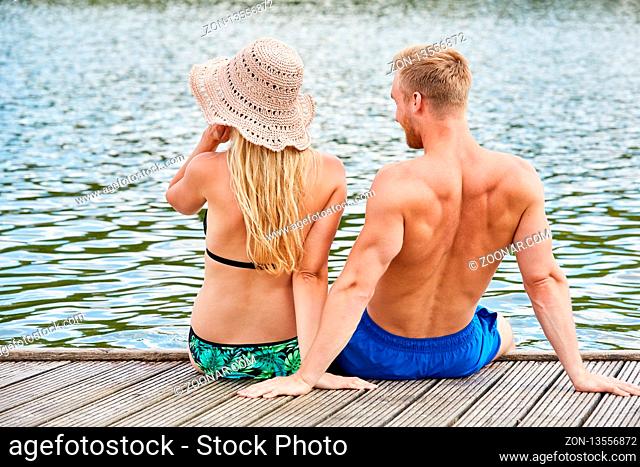 Junges Paar im Sommerurlaub sitzt auf einem Steg am See und genießt die Natur