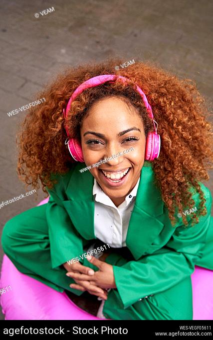Happy businesswoman listening music through wireless headphones sitting on inflatable ring