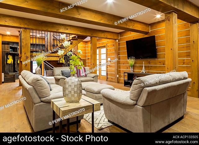 Beige suede sofas, love seat and ottomans in family room with thick wood block end tables and staircase inside a milled Eastern white pine timber and flat log...