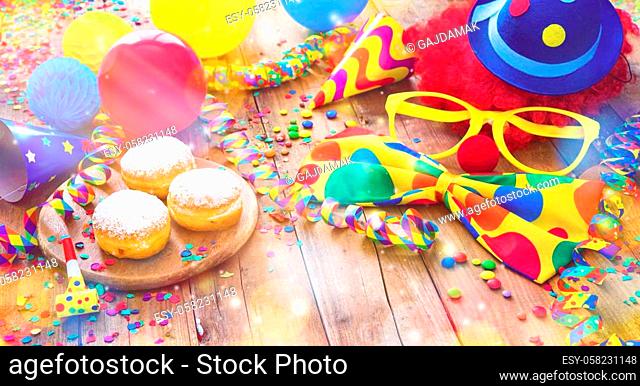 Colorful carnival or party background with donuts, balloons, streamers and confetti and funny face formed from wig, nose and glasses on rustic wooden planks...