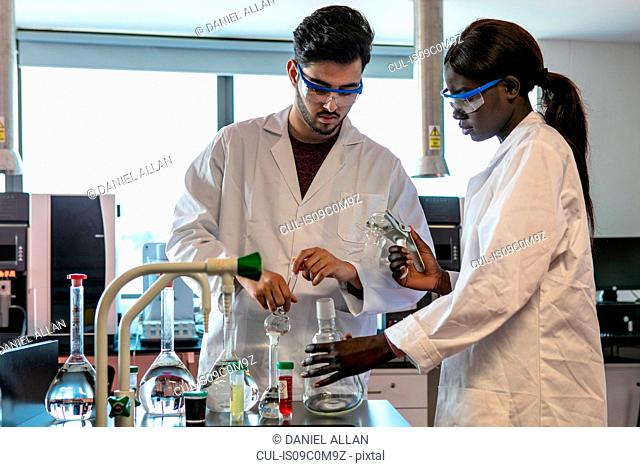 Young male and female scientists preparing experiment with sample bottles in laboratory