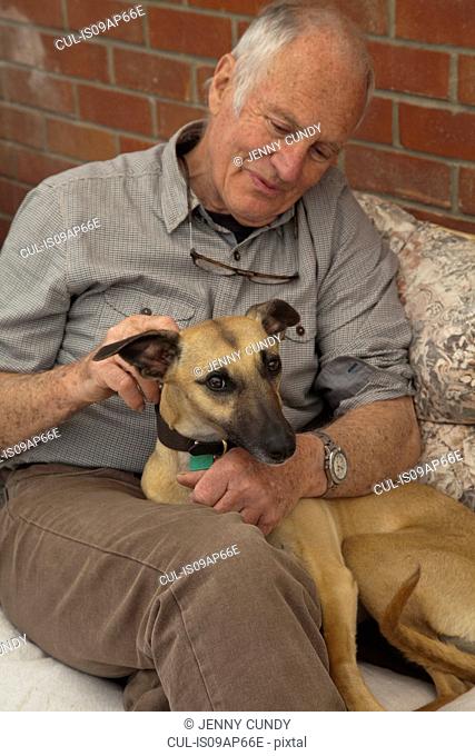 Senior man, sitting, stroking pet dog