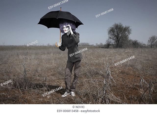 Funny man in the steppe holding umbrella and looking beyond the horizon. Artistic darkness and colors added