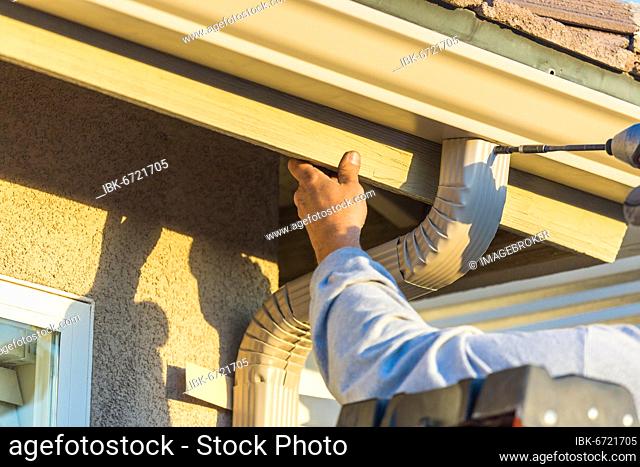 Worker attaching aluminum rain gutter and down spout to fascia of house