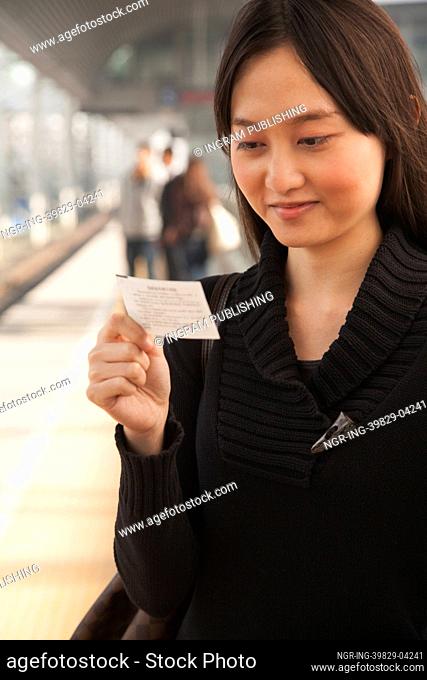Young Woman Looking At Train Ticket on Railroad Platform