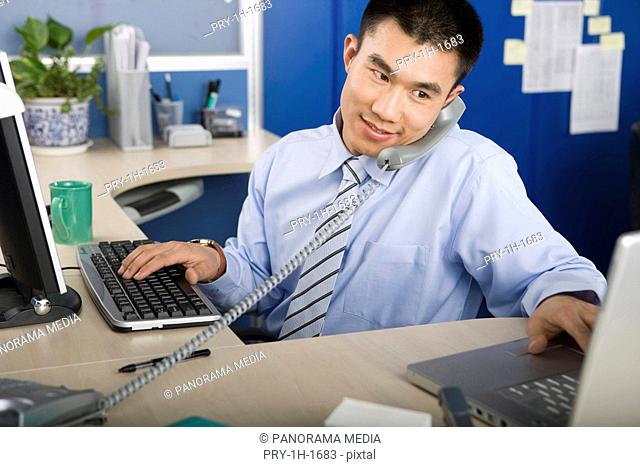 Businessman at desk using telephone and laptop