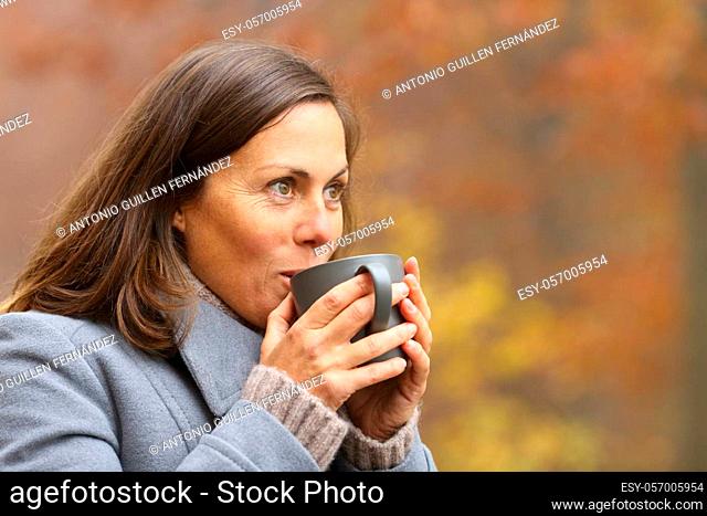 Adult woman drinking coffee standing in a park in autumn contemplating views
