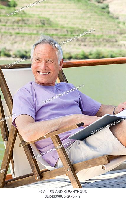 Senior man reading book on a boat holiday