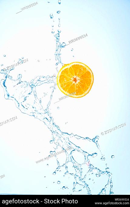 Half of orange fruit with water splash in midair, isolated on light blue background. Refreshment concept