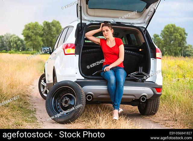 Young sad woman sitting in broken car at countryside