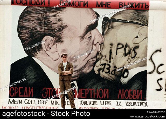 August, 1990. Berlin, German Democratic Republic. Soviet artist Dmitry Vrubel stands at his graffiti painting My God, Help Me to Survive This Deadly Love
