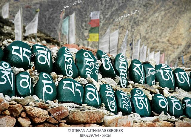 Tibetan script on green painted stones set in a row in front of prayer flags at monastery Tashi Gompa Phu Nar-Phu Annapurna Region Nepal