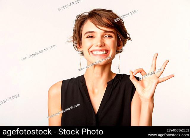 Close-up of satisfied attractive woman showing okay gesture and smiling pleased, approve something good, standing white background