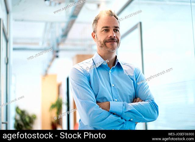 Thoughtful businessman with arms crossed standing in corridor at workplace