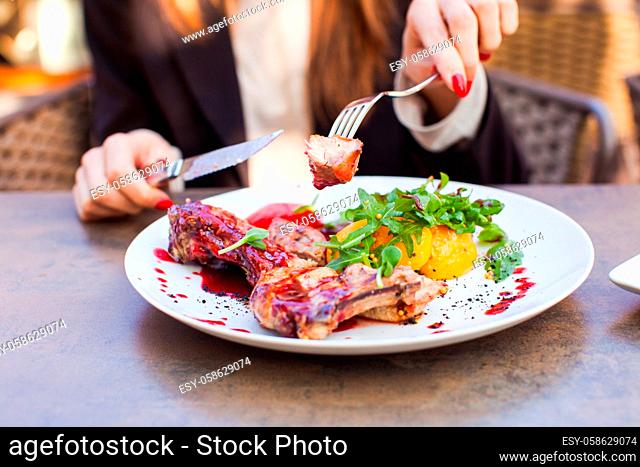 Woman eat healthy lunch in restaurant. Grilled meat steak with cranberry sauce, glazed peaches and arugula salad on white plate