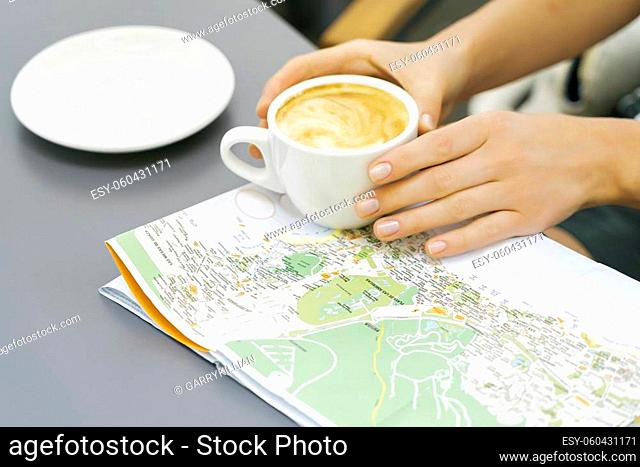 Woman hands hold coffee cup over the map on the table. travel Canary islands and looking for a new place to visit. Sunny day in a street cafe