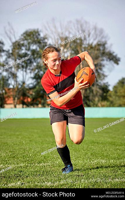 Determined girl running with rugby ball on field