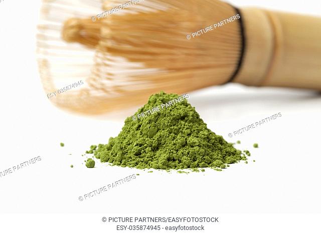 Heap of powdered green matcha tea and chasen on white background