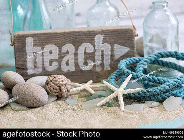 Nautical still life with wooden beach sign, rope, pebble and old blue bottles