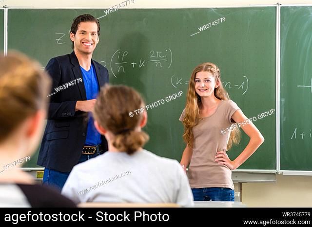 School class Teacher or educator testing in a lessons students in front of the class at the blackboard or board or chalkboard in math