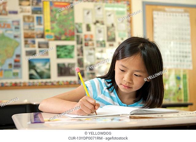 pupil writing in book at desk in classroom
