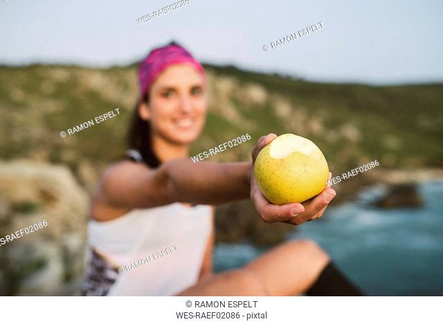 Sportive woman sitting on rocks, holding apple, focus on foreground