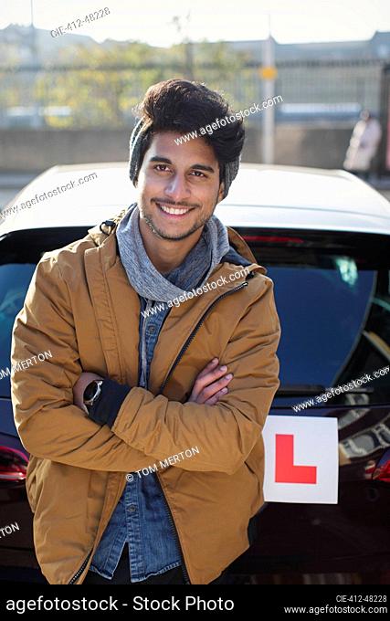 Portrait confident young man with learners permit leaning against car