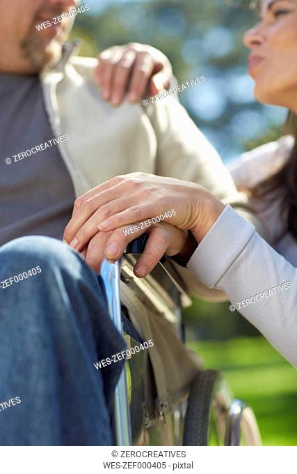 Woman holding hand of man in wheelchair