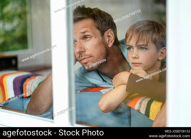 Father and son leaning on sofa seen through glass window