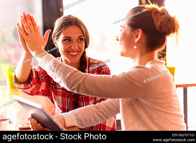 Toned image of beautiful girls giving highfive while spending free time in cafe or restaurant and communicating or talking about every day things