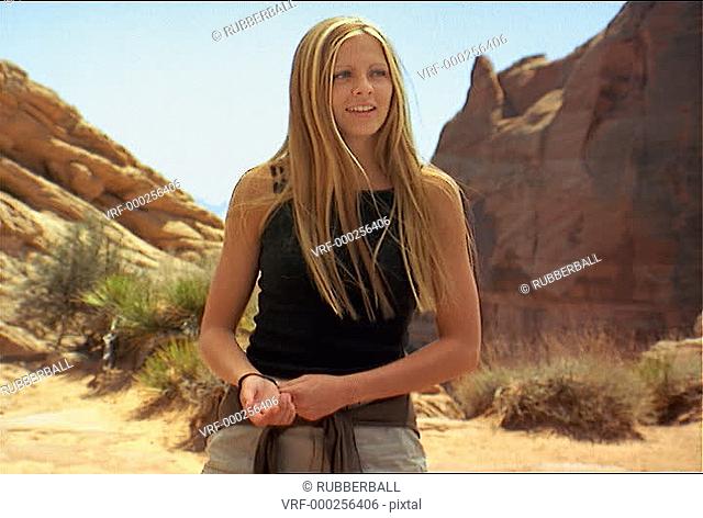 medium shot of a young attractive caucasian female in a red rock canyon as she attempts to dance and laughs
