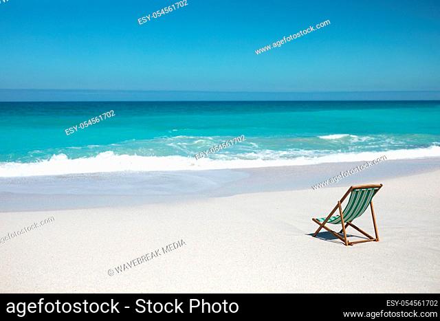 Rear view of an empty deckchair sitting on a beach, facing the sea and the horizon. Weekend beach vacation, lifestyle and leisure