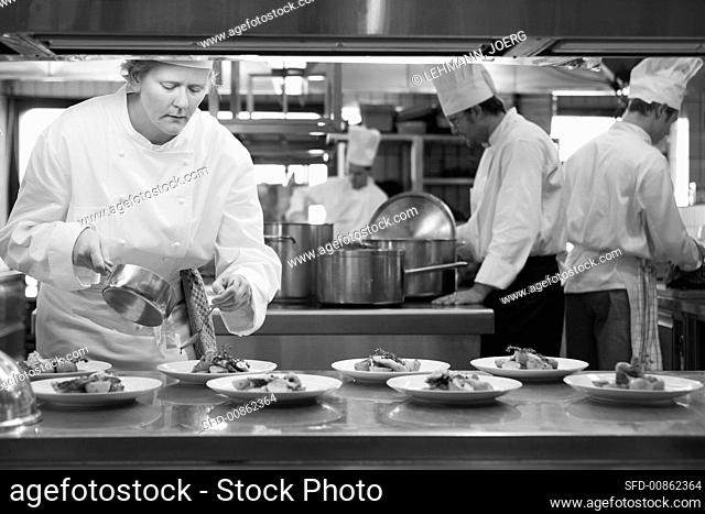 Female chef pouring sauce over main courses