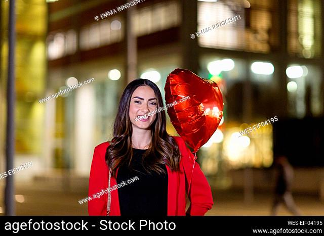 Smiling woman holding heart shape balloon at night