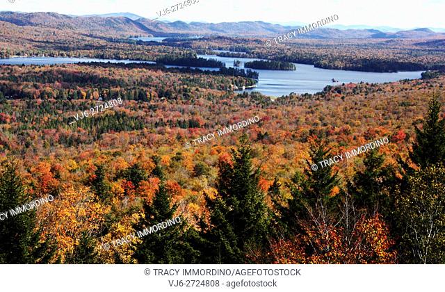 View of forest in stunning fall foliage with Gray Lake and mountains in the background from the top of Mount Mccauley in Old Forge, NY, USA