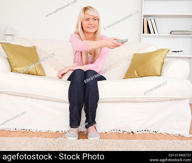 Good looking blonde female watching tv while sitting on a sofa