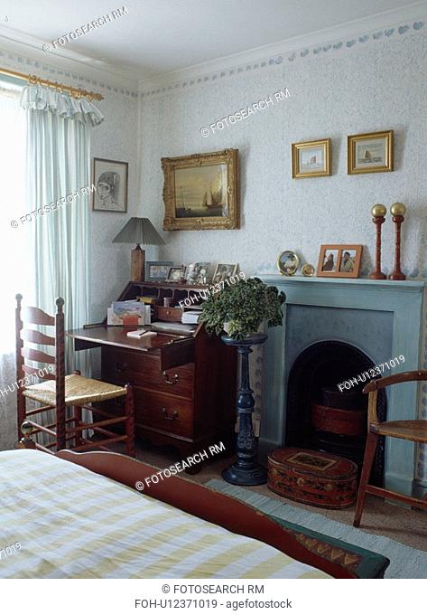 Antique desk and rush-seated ladderback chair in small bedroom with pale blue fireplace
