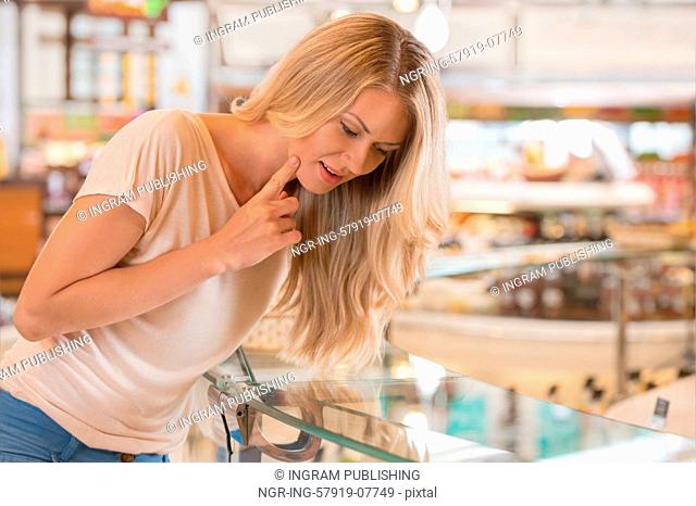 Woman shopping at the supermarket, standing near glass showcase and thinking what to choose