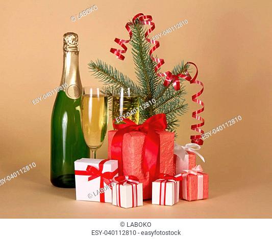 Fir-tree branch, bottle and wine glasses with champagne, big and small gift boxes on a beige background