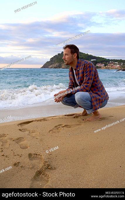 Man crouching on sand at beach