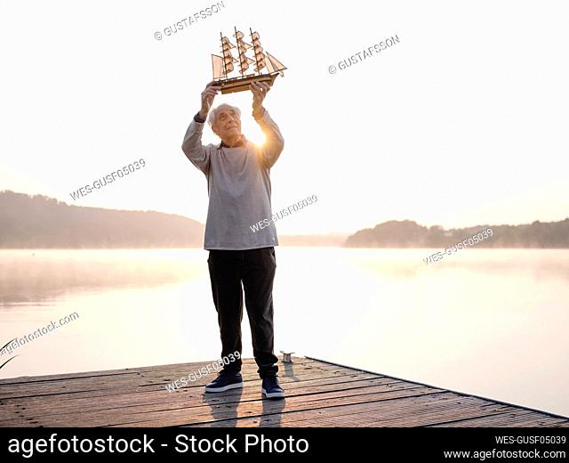 Senior man playing with ship toy while standing on pier