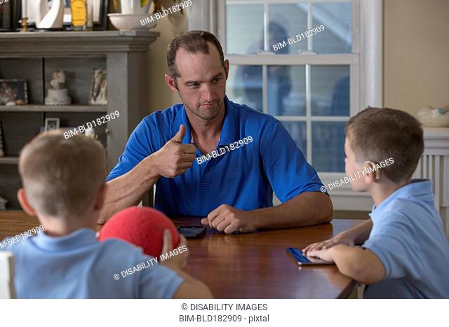 Caucasian father and sons signing at dinner table