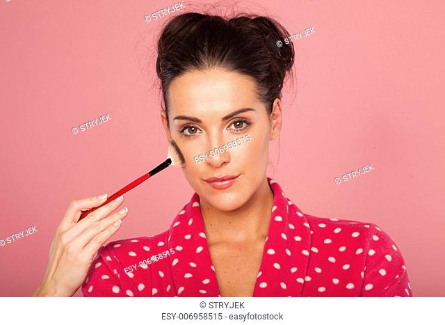 Glamorous woman applying blusher with a large soft bristle cosmetics brush to contour her cheekbones