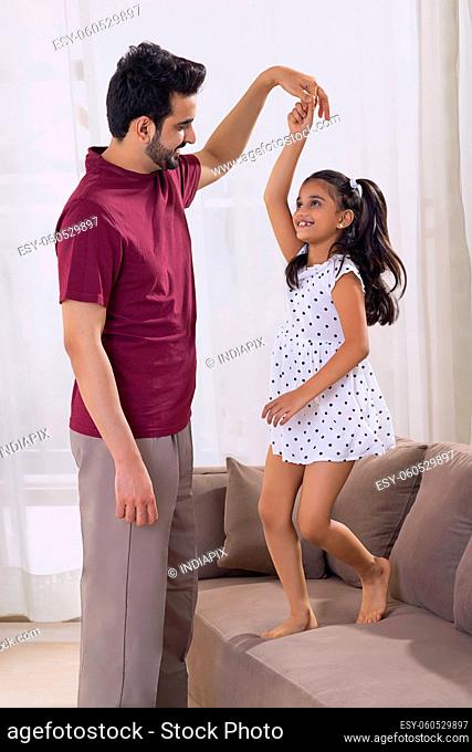 A HAPPY DAUGHTER DANCING AT HOME WITH FATHER
